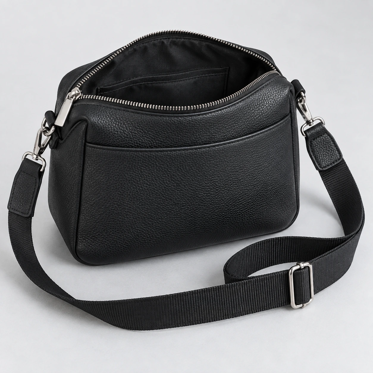 Bolsa transversal preta ilustrativa, com zíper aberto, bolso interno e alça ajustável visíveis